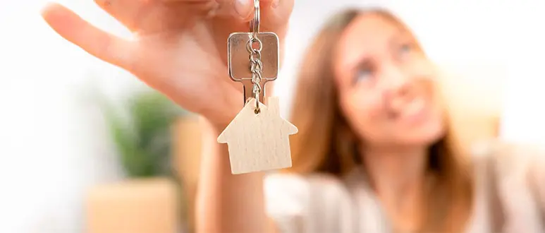 Een vrouw die de sleutels van haar nieuwe appartement vasthoudt aan een sleutelhanger in de vorm van een huis.