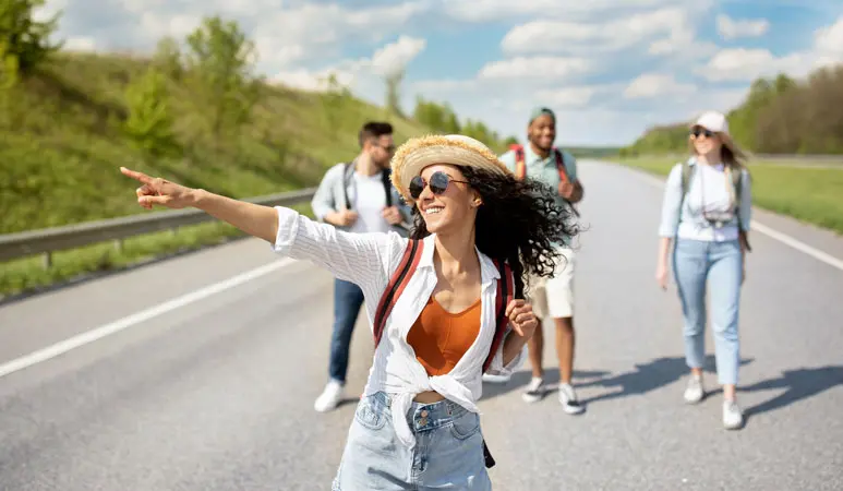Grupo de viajeros con mochila caminando por una carretera soleada