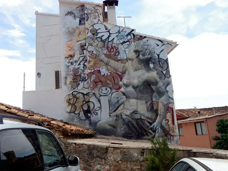 Graffitimuurschildering in Fanzara met een klassiek standbeeld op een witte muur