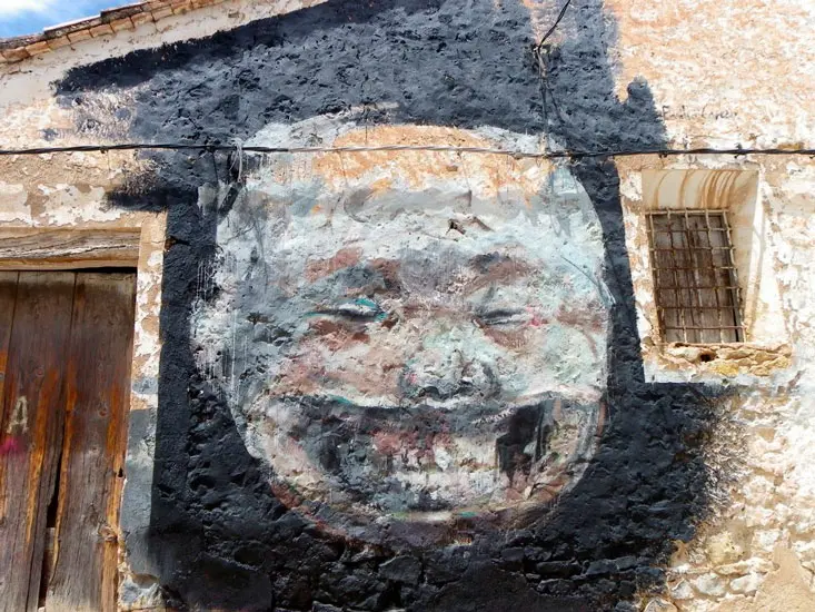 Graffiti in Fanzara met de afbeelding van een lachende maan, geschilderd op een oude muur met een zwarte achtergrond