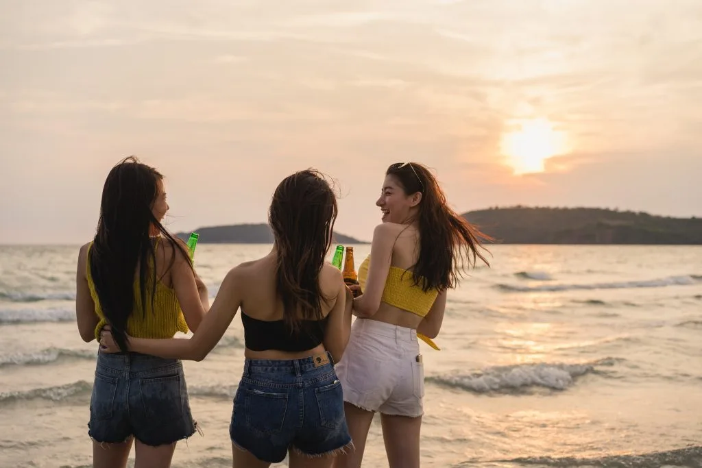 Tres amigas de espaldas, charlando en la orilla del mar con el sol bajo en el horizonte