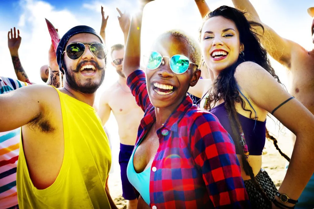 Grupo de amigos riendo con los brazos en alto en una fiesta en la playa