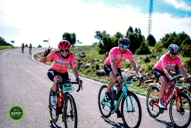 Fietsers in roze shirts die deelnemen aan een wielerwedstrijd in Oropesa, terwijl zij over een weg met een natuurrijk landschap fietsen.