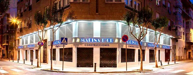 Fachada iluminada de un edificio en la Calle Moyano, Castellón, con el local de Marina d'Or Construcciones