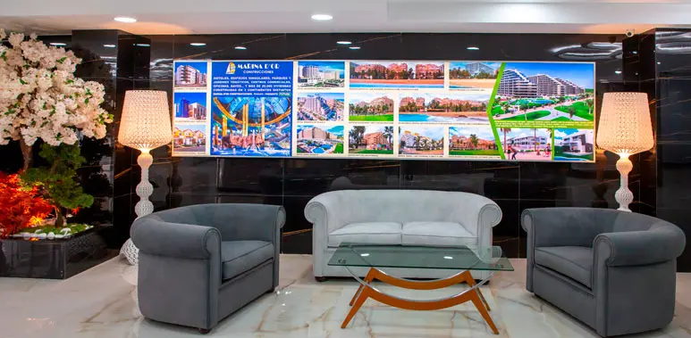 Sala de espera moderna con sofás y paneles promocionales en el piso piloto de Marina d'Or, Calle Moyano, Castellón.