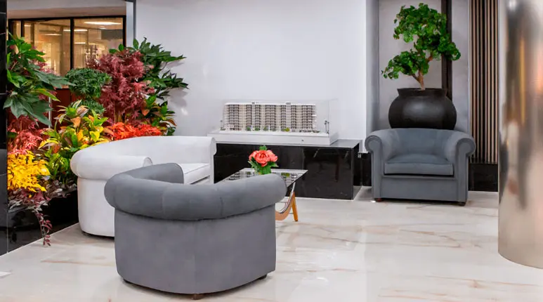 Sala moderna con sofás, plantas decorativas y una maqueta arquitectónica en el piso piloto de Marina d'Or en la Calle Moyano, Castellón.