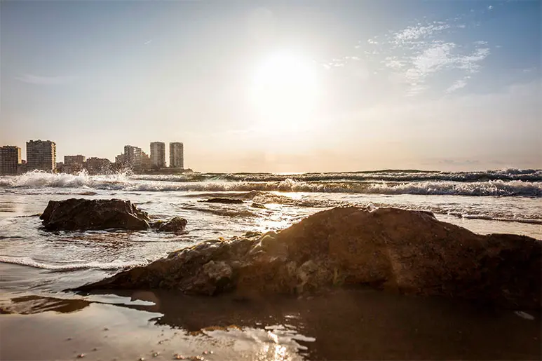 Playa de La Concha en Oropesa del Mar con rocas, edificios de fondo y un amanecer espectacular